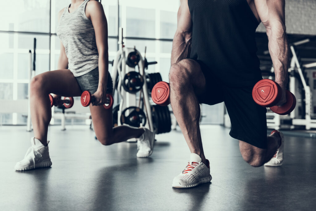 A couple doing lunges with dumbbells during a training session in the gym.