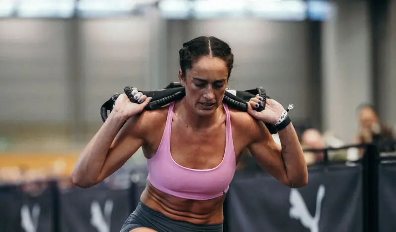 A female athlete working out and doing sandbag lunges in a gym.