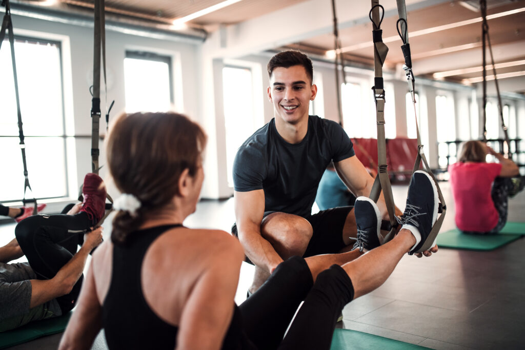 Trainer assists an athlete using suspension straps during a workout, guiding her form while they interact in a fitness studio.